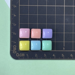 Size reference of glossy square resin beads in pastel colors on a centimeter scale mat