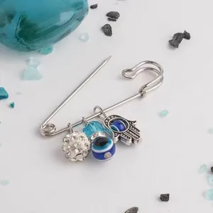 Detailed shot of silver pin brooch with crystal ball and blue evil eye Hamsa pendants