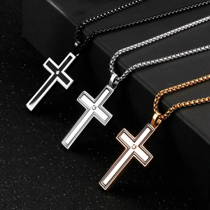 Three men's cross necklaces in black, silver, and gold steel on a textured display