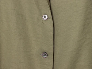 Détail macro du tissu texturé vert olive et des boutons sur cet ensemble femme