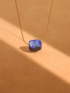 Artistic detail of gold chain necklace with rectangular blue turquoise pendant in sunlight