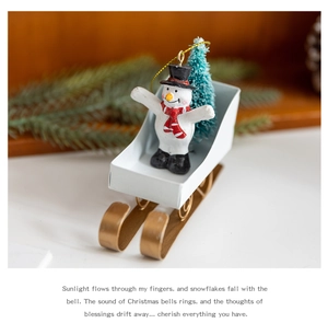 Detail of a white snowman in a sleigh with a mini Christmas tree and gold hangers