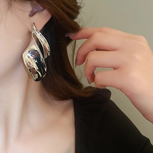 Close-up of a silver irregular wave earring with a high-shine metallic finish on a model