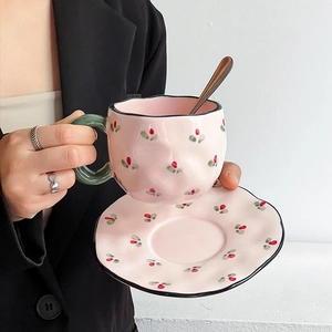 Detail of pink ceramic coffee cup with green handle and red flowers, holding a silver spoon