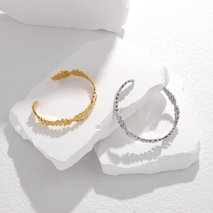 Dettaglio dei bracciali aperti a foglia d'ulivo in oro e argento su pietre bianche