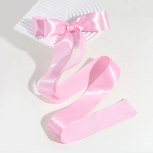 Detail shot of a pink satin bow hair clip on a white decorative wave plate