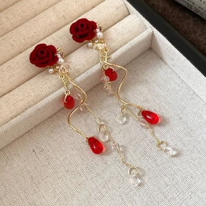 Close-up of velvet rose earrings with gold spiral tassels and red teardrop glass charms