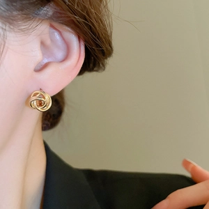 Close-up of elegant gold twisted knot stud earrings worn by a model in soft lighting