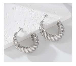 Detail of silver twisted C-shaped earrings on white stone, minimalist geometric design
