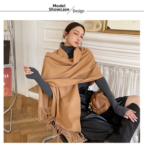 Model wearing a large camel faux cashmere scarf with tassels in a warm indoor setting