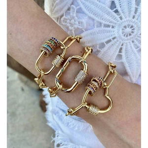 Dettaglio di bracciali a catena dorata con ciondoli a moschettone e pietre colorate