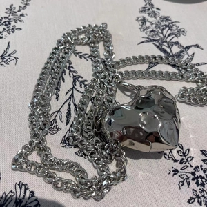 Detail of silver heart charm on chunky chain necklace over a floral background