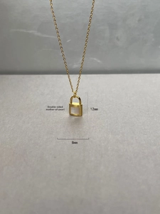 Macro detail of lock pendant featuring double-sided white mother of pearl inlay and gold finish