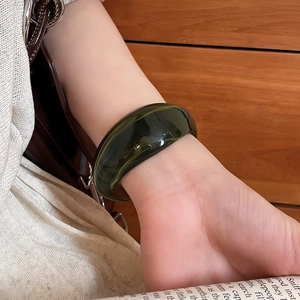 Close-up of a dark green transparent acrylic wide bangle worn by a model in a minimal setting