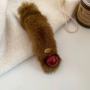 Detail of plush brown acrylic hair clip with Lucky metal plate on white knit sweater