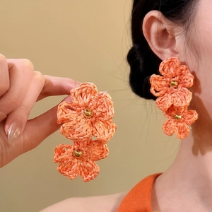 Close-up detail of handmade orange woven flower earrings in Bohemian vacation style.