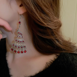 Macro side view of vintage peacock drop earrings with red crystals on a female model