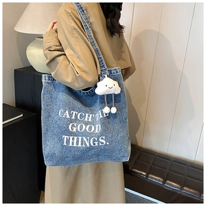 Detail van blauwe denim draagtas met witte letters en schattige wolkenhanger