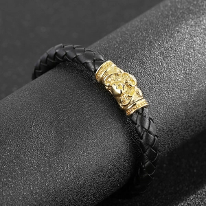Braided black leather bracelet with gold skull cylinder magnetic clasp on display stand