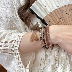 Detail of bohemian layered beaded bracelets with tassels on a lace clothing background