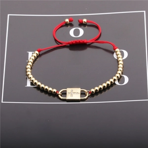 Macro shot of red braided cord bracelet with gold beads and a zircon cross pendant