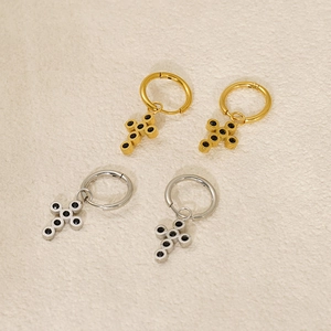 Detailed view of gold and silver cross earrings with black center on textured beige background