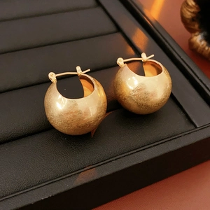 Close-up of golden textured huggie hoop earrings on a black jewelry display tray