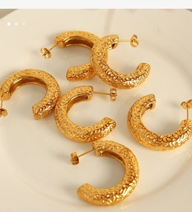 Macro shot of gold C-shaped earrings with hammered texture on white ceramic plate