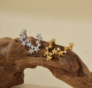 Macro shot of silver and gold star earrings with tiny zircon stones on wood surface