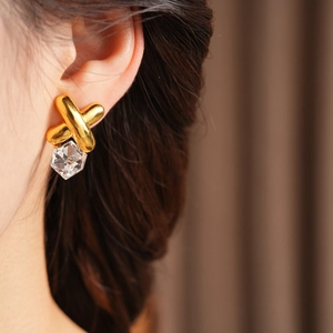 Detail of vintage gold X-shaped earrings with clear geometric crystal on a model
