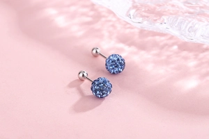 Macro shot of blue crystal pavé ball earrings with silver screw backs on pink background