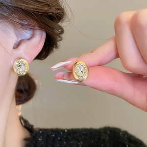 Detailed close-up of oval gold brushed earrings with zircon inlay worn by a model