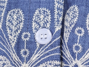 Détail d'une broderie florale blanche sur tissu bleu avec bouton blanc de robe