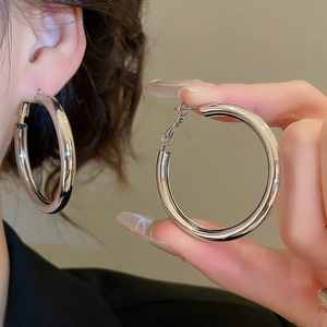 Detail of large silver hoop earrings with polished finish on model and held by hand