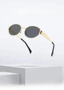 Detail of gold oval metal sunglasses with dark gray lenses on a minimalist white stand
