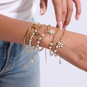 Détail de bracelets superposés en acier doré avec breloques fleurs et perles colorées