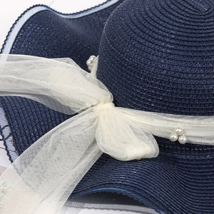 Close-up of a blue straw sun hat featuring a white mesh bow and artificial pearl details
