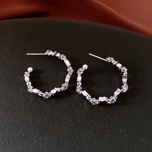 Macro shot of silver C-shaped hoop earrings featuring geometric zircon stones on black velvet