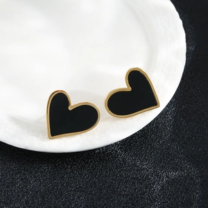 Macro detail of black heart studs with gold edges on white ceramic, elegant fashion jewelry