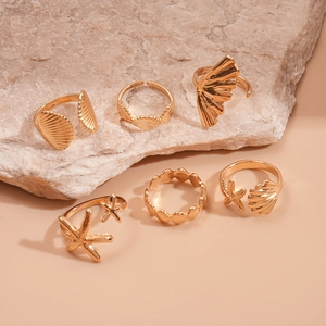 Detailed view of 6-piece gold starfish and seashell rings on a textured stone surface