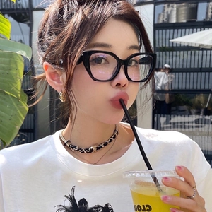 Close-up of black cat-eye glasses frames on a model in an outdoor cafe setting