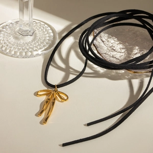 Close-up of golden bow pendant necklace with black velvet ribbon on beige surface