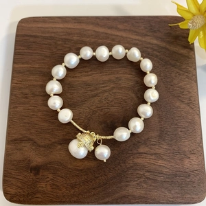 Macro detail of Baroque freshwater pearl bracelet with a golden lucky cat charm on wood