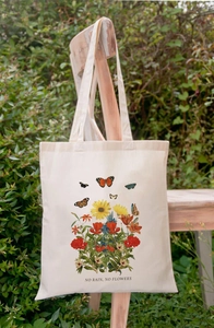 Cream canvas tote bag with No Rain No Flowers floral print hanging on a wooden chair
