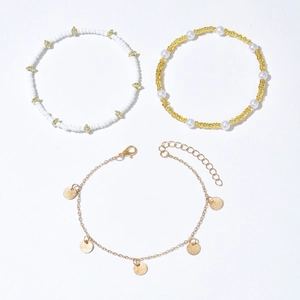 Three-piece bohemian anklet set with white beads, gold discs, and pearls on white background