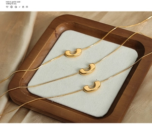 Vue macro du collier avec pendentif en U plaqué or et chaîne serpent sur coussin blanc
