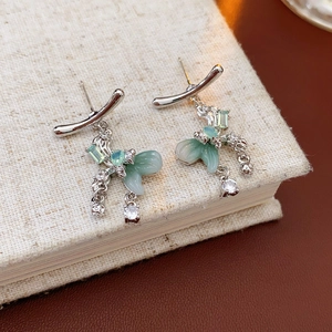 Detail of silver bow tassel earrings with green stones and sparkling cubic zirconia