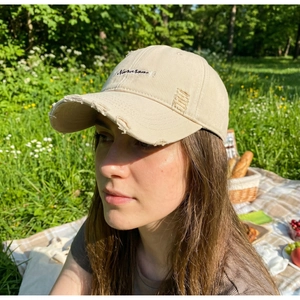 Detailed shot of frayed distressed edges and Newason embroidery on a beige cotton cap
