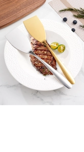 Silberne und goldene Edelstahl-Pfannenwender auf weißem Teller mit gebratenem Steak