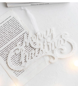 Close-up of white glitter Merry Christmas hanging ornament with silk ribbon on vintage paper